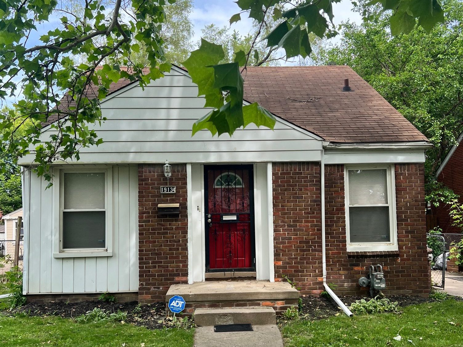 Front view of a charming brick house with a red door, surrounded by green trees and grass.